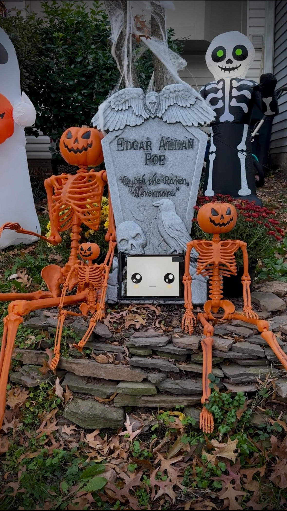 A headstone with a tablet at the bottom next to two orange skeletons with pumpkins as heads.